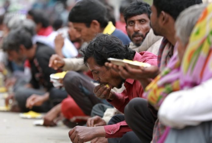 Indios pobres y sin hogar comen alimentos repartidos por el gobierno de Delhi en Nueva Delhi, India, el jueves 26 de marzo de 2020. (AP Foto)
